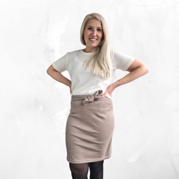 Sara merinovillahame taupen värisenä kuvattuna suoraan edestä mallinpäällä. Vyötärölle on sidottu zerowaste merinovillavyö rusetille. Mallilla on valkinen paita ja kädet lanteilla.